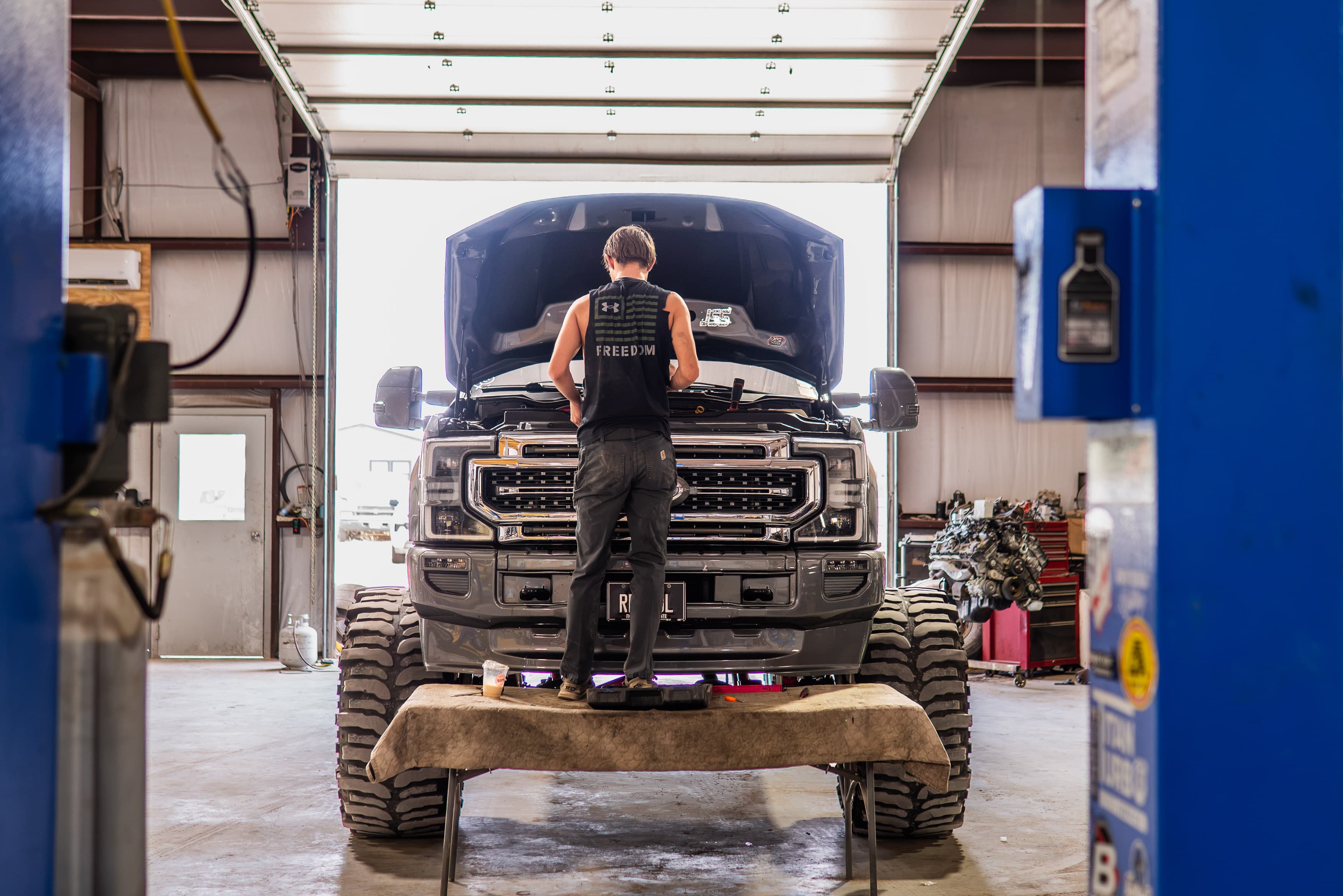 Technician working under the hood of a lifted diesel pickup in the shop
