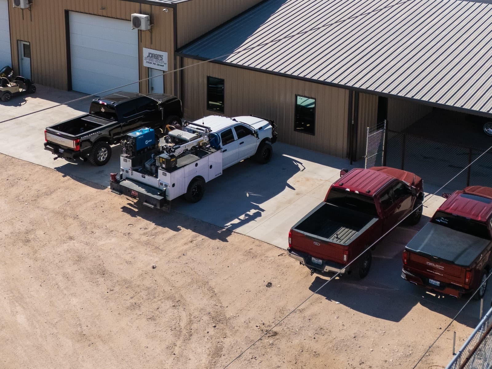 Work trucks parked at the shop, including a service body with a welder